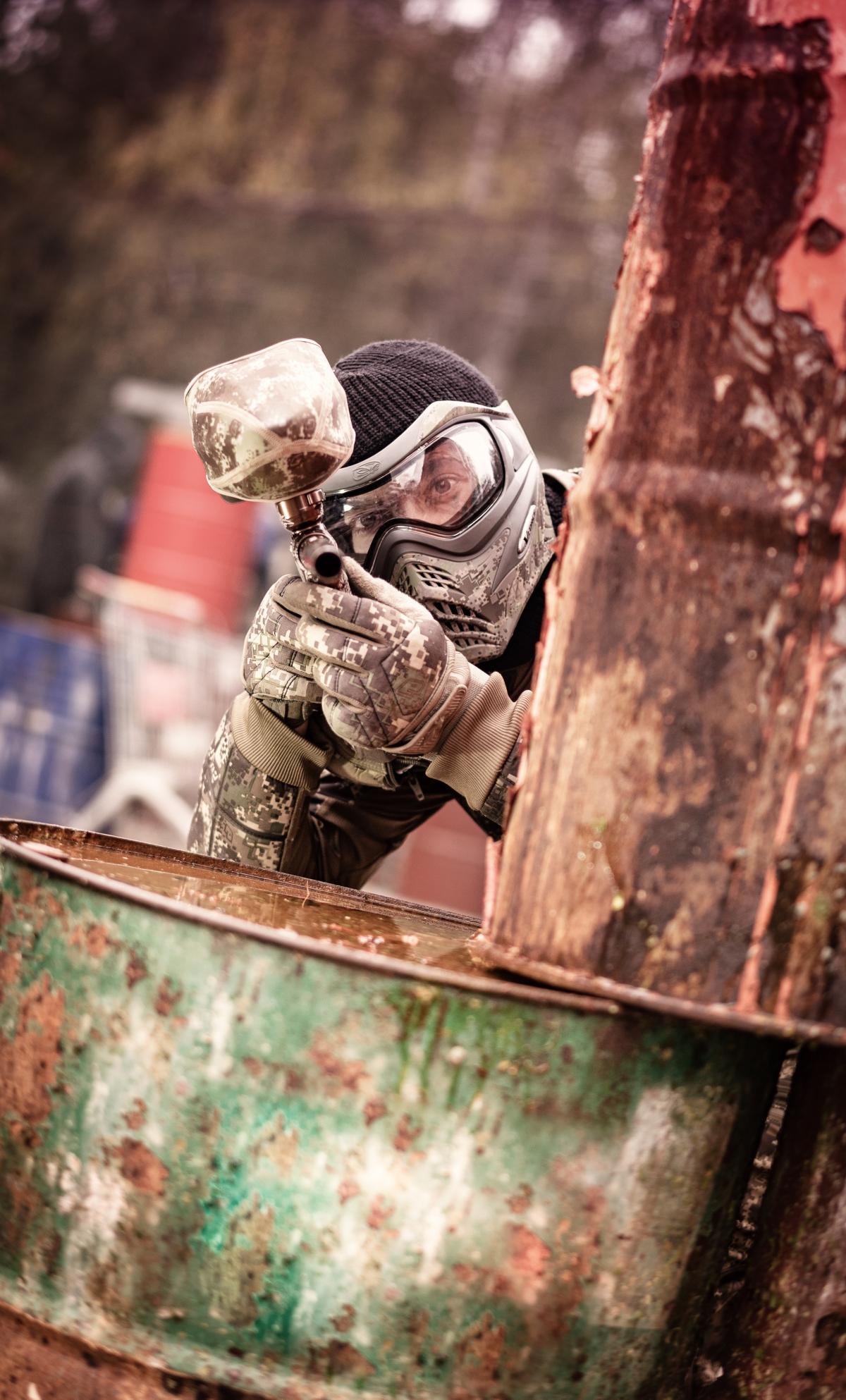 Ein Paintballspieler im Freigelände in Deckung hinter verrosteten Tonnen