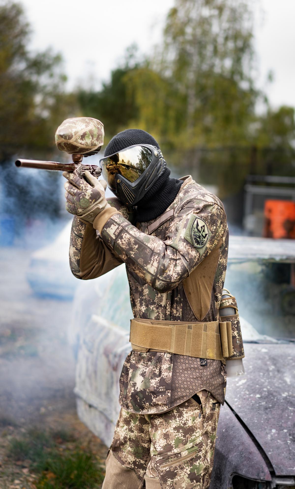 Ein Paintballspieler im Freigelände vor einem verrosteten Auto