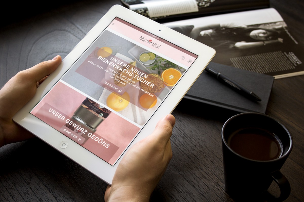 Die Webseite von Paulikocht auf einem Tablet-PC, der vor einem Schreibtisch in Händen gehalten wird